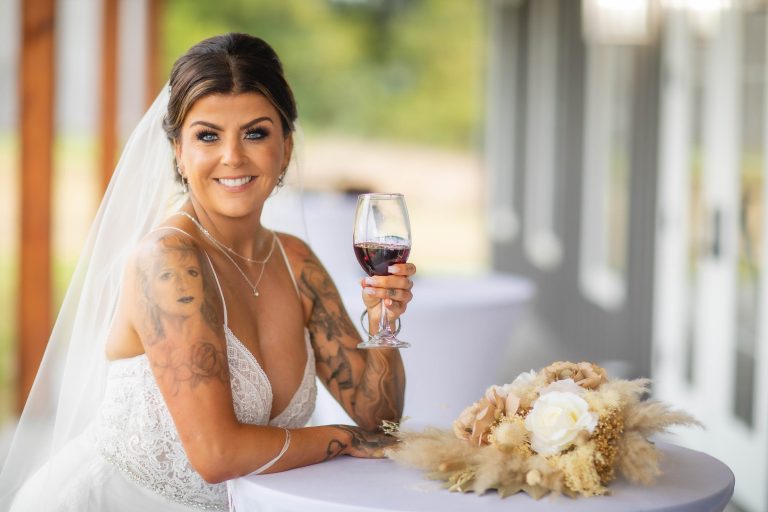 A bride with tattoos holding a glass of wine at Two Lions Vineyard in Upper Marlboro, Maryland.