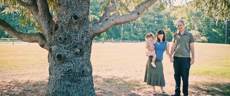 A family is standing in front of a tree at Watkins Park.