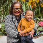 An AfricanAmerican woman holding a child in front of flowers at the National Portraits Gallery, capturing a touching family moment.