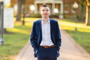 A young man in a blue suit standing on a brick path for his graduation portrait.