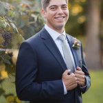 A man in a suit is smiling in front of a fence at Fleetwood Farm Winery.