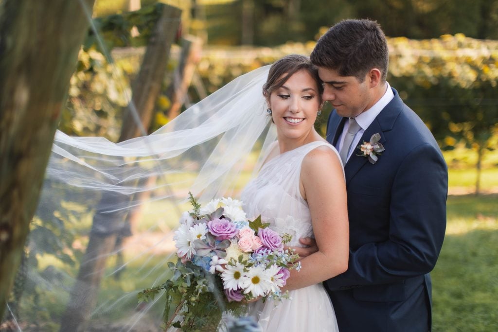 A wedding portrait of a bride and groom embracing in the stunning vineyard of Fleetwood Farm Winery.