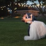 A bride and groom sharing a romantic portrait at Fleetwood Farm Winery during their wedding, as they passionately kiss under the soft glow of string lights in the lush grass.