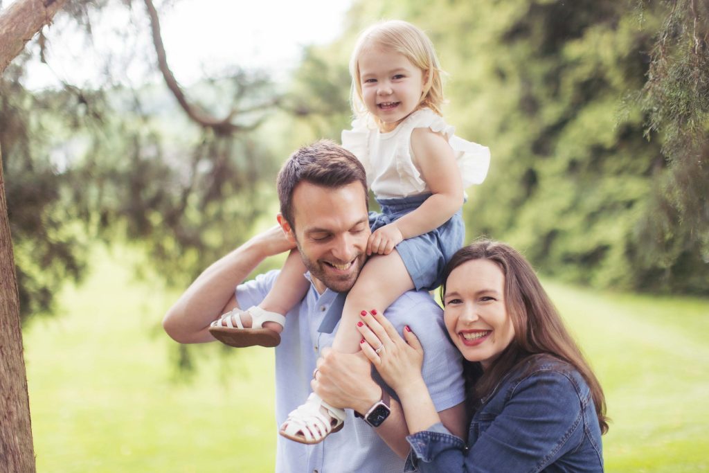 A family is holding their daughter in their arms for portraits in a park.