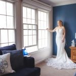 A candid bride prepares for her wedding in front of a window in her bedroom.