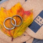 Wedding rings on a cork board adorned with fall leaf.