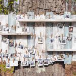 A wooden board with wedding pictures hanging on it in the woods.