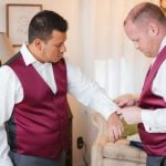 Two men candidly adjusting their vests during wedding preparation.