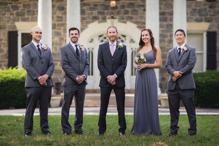 A wedding portrait of groomsmen and bridesmaids in front of a mansion.