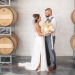 A wedding portrait featuring a bride and groom in front of wine barrels.