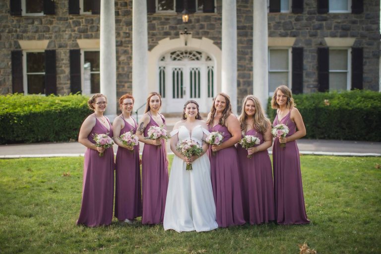 A group of bridesmaids posing for a wedding portrait in front of a mansion.