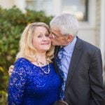 An older couple posing for a wedding portrait in front of a house.