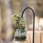 A detailed wedding centerpiece: a vase filled with flowers on a table in a wooded area.