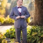 A groom in a gray tuxedo poses for a wedding photo.