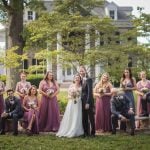 A wedding group poses for a portrait in front of a mansion.