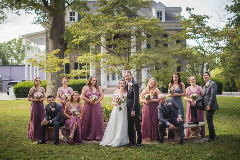 A wedding group poses for a portrait in front of a mansion.