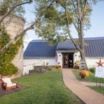 A detailed wedding scene featuring a white barn, chairs, and a tree.