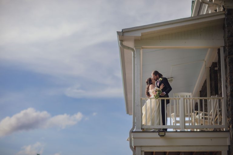 A wedding portrait of a bride and groom kissing on the porch of a house.