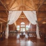 A detailed wedding reception in a barn with white drapes and chandeliers.