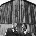 Wedding portrait of two grooms standing in front of a barn.