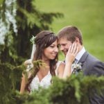 A portrait of a bride and groom embracing in a grassy field at their wedding.