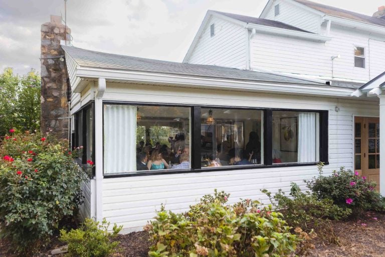 A group of people are sitting outside of a house during a wedding reception.