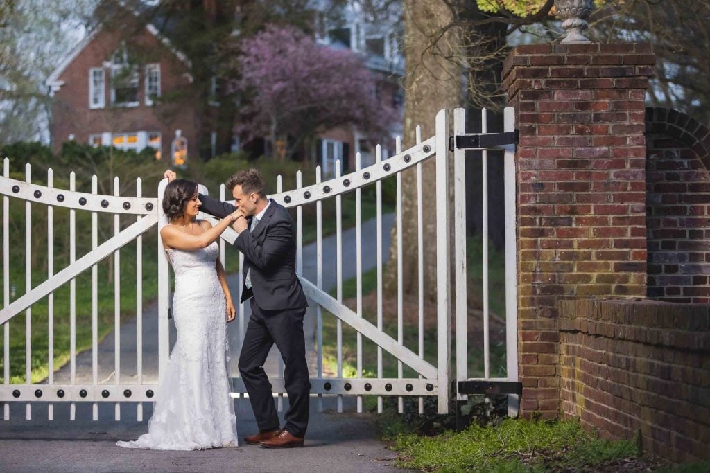 A bride and groom kiss in front of a white gate, creating a beautiful wedding portrait.