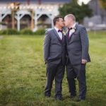 Wedding portrait of two grooms kissing in front of a barn.