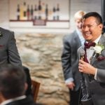 Two men in suits laughing at each other at a wedding reception.