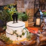 A detailed wedding cake sits on a table next to a fireplace.