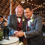 Two men cutting a wedding cake at a reception.