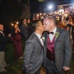 Two grooms kissing at their wedding reception.