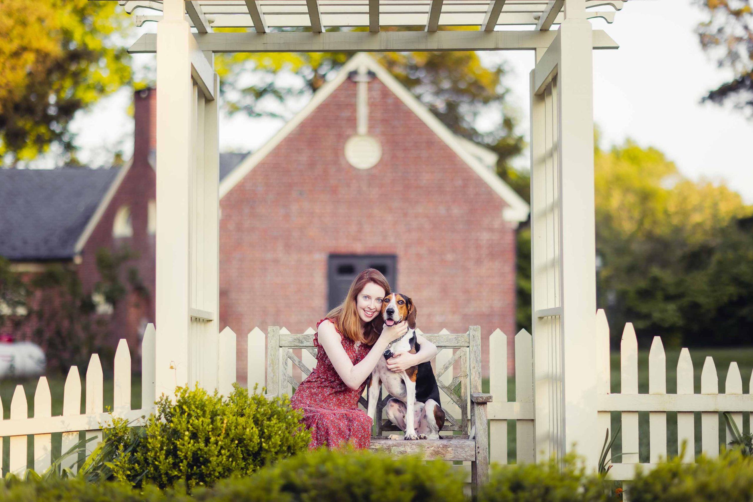 A woman poses for a dog portrait on a wooden bench at Montpelier Mansion.