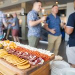 A group of people celebrating at a birthday party gathering around a platter of food.