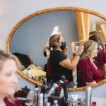 A candid bride preparing for her wedding, getting her hair done in front of a mirror.