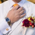 A man is adjusting his boutonniere for a wedding portrait.