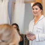 A candid bride preparing for her wedding with her bridesmaids in front of a mirror.