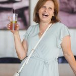 A woman smiling at a birthday party while holding a drink.