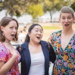 Three women with their mouths open at a lake during a birthday party.