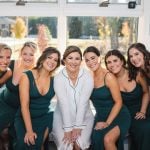 Bridesmaids in emerald dresses candidly posing for a photo during wedding preparations.