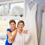 Candid bridesmaids posing in front of a wedding dress during preparation.