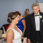 A candid wedding preparation moment captured of a man in a tuxedo and a woman in a dress.