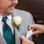 A candid man in a suit preparing for a wedding by putting on a boutonniere.