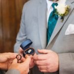 A man is putting a ring on a man's finger during a wedding ceremony.