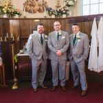 Three groomsmen candidly standing in front of a church during wedding preparation.