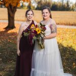 Two bridesmaids posing for a portrait in front of a fall tree at a wedding.