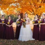 Burgundy bridesmaids posing in front of fall leaves at a wedding.