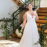 A bride in a white wedding dress standing in front of a staircase, captured in a stunning portrait.