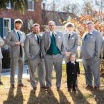 A group of groomsmen pose for a wedding portrait in front of a house.