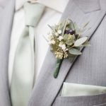 Detailed wedding attire showcasing a man in a grey suit with a green boutonniere.